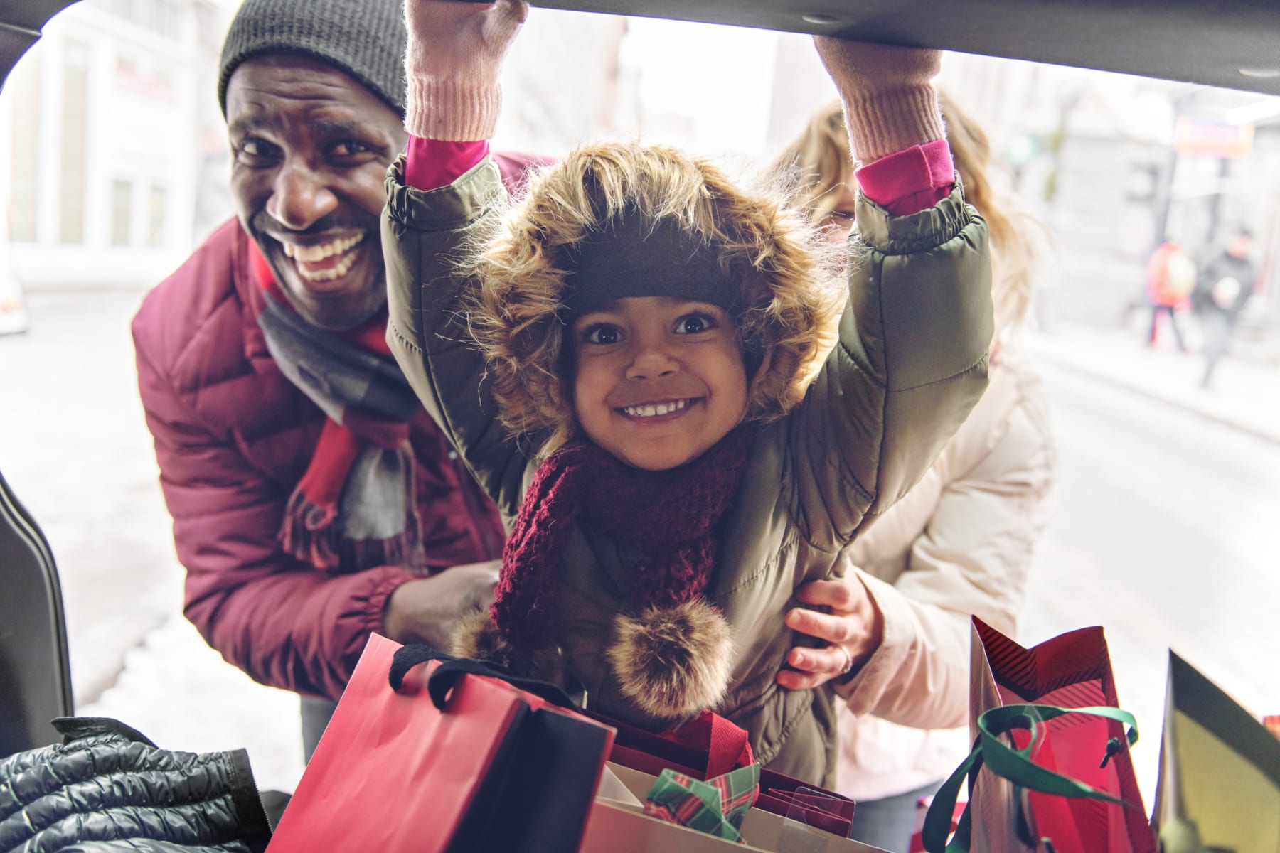 Family poses with holiday shopping bags in trunk of vehicle.